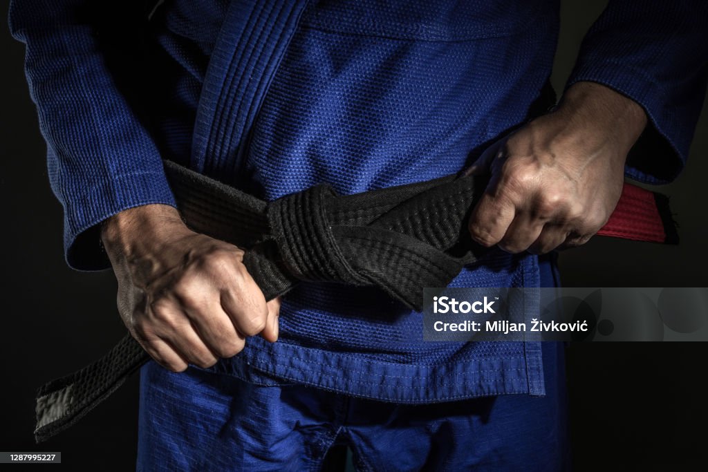 kimono azul com a faixa preta sendo amarrada na cintura.